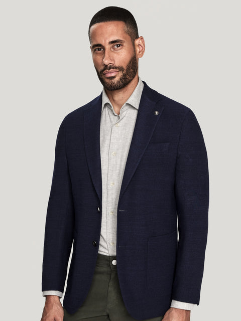 Man wearing a navy blazer over a light gray shirt with olive pants.