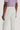 Cream-colored chino pants with button closure and back pocket detail on model wearing lavender shirt.