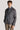 Man wearing grey herringbone shirt jacket with blue collar over beige trousers.
