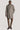 Man wearing taupe twill topcoat with cream inner collar over brown trousers and burgundy boots.