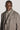 Man wearing taupe two-tone twill topcoat with high collar and removable bib insert, single button closure.