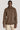 Brown long-sleeve polo shirt with collar and button placket, worn with cream-colored trousers.