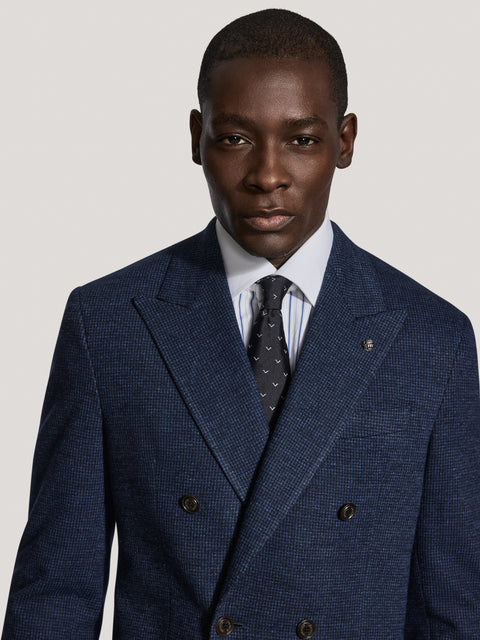 Navy double-breasted blazer with micro houndstooth pattern worn over white dress shirt and dark tie.