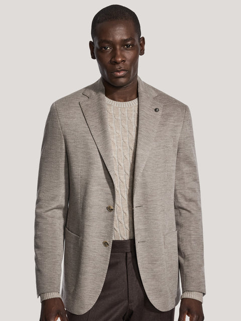 Light taupe herringbone blazer with notch lapels and button closure, worn over cream cable-knit sweater.