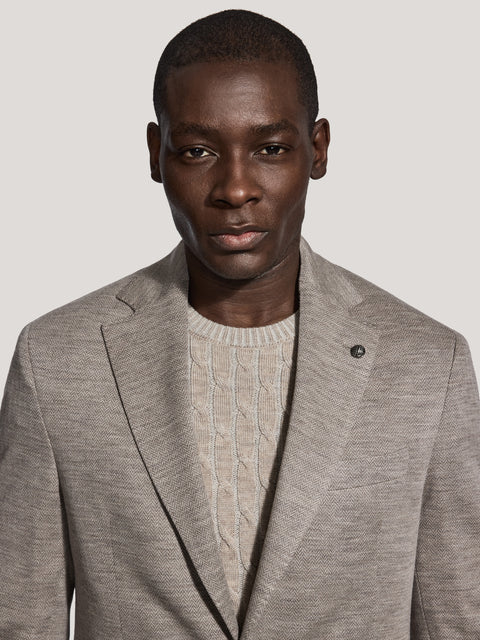 Light taupe herringbone blazer with notch lapels worn over cream cable-knit sweater.